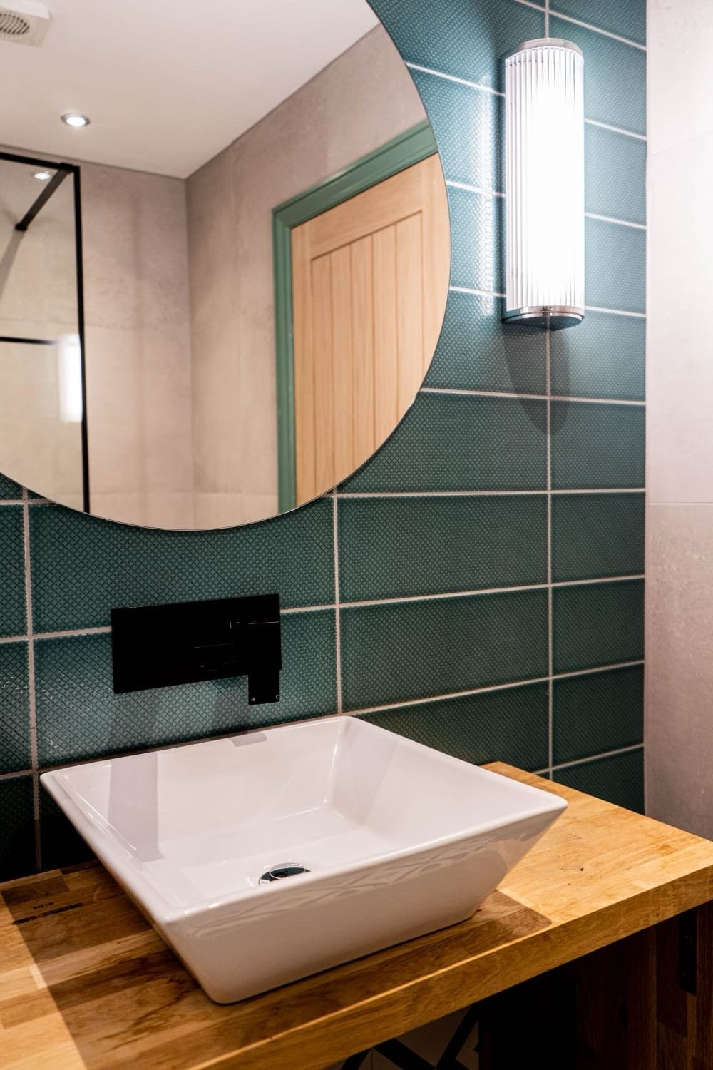Jacobean Hotel bathroom with green tiles, oak vanity and round mirror